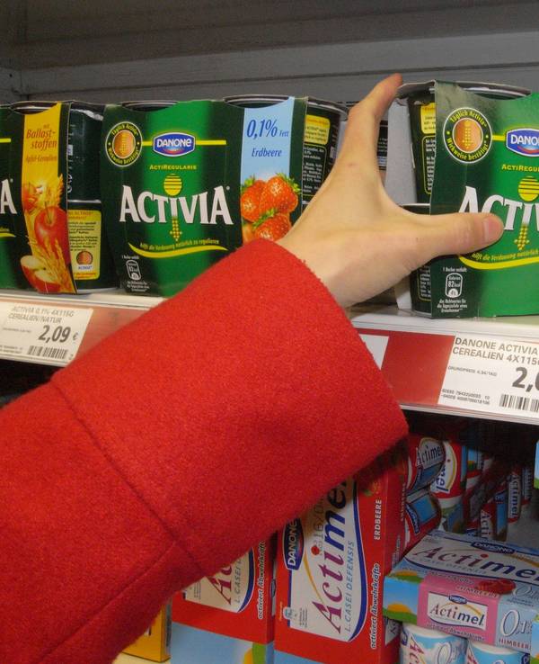 Eine Hand greift nach Danone-Joghurt im Kühlregal.