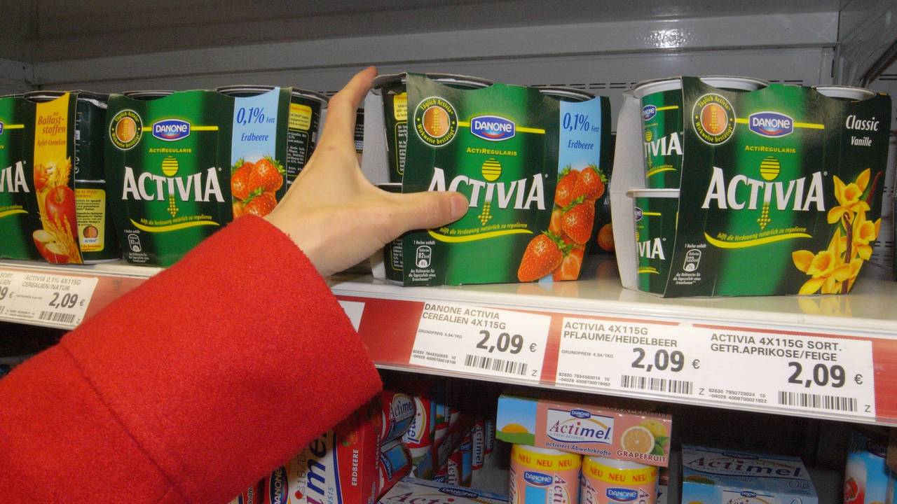 Eine Hand greift nach Danone-Joghurt im Kühlregal.