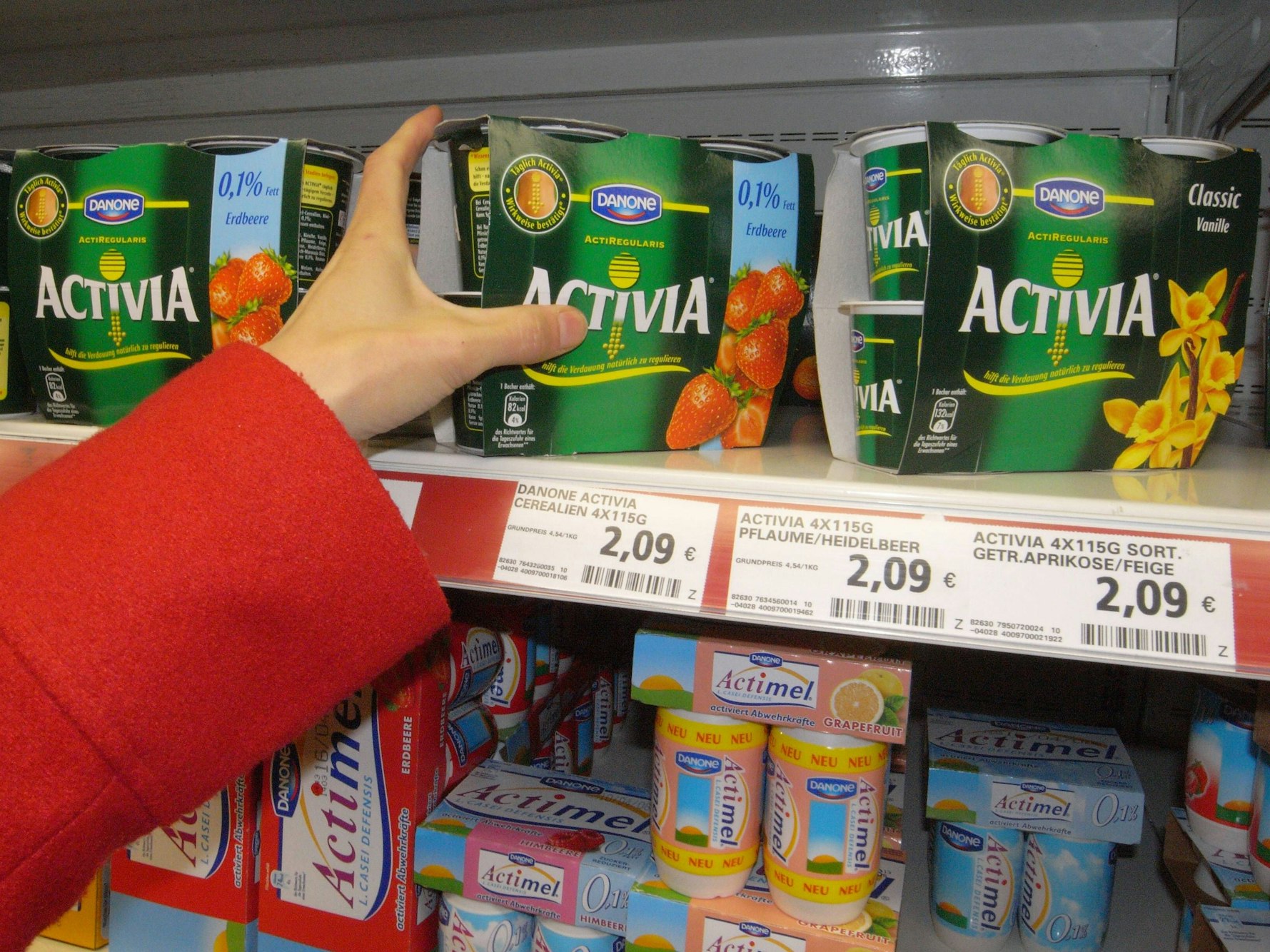 Eine Hand greift nach Danone-Joghurt im Kühlregal.