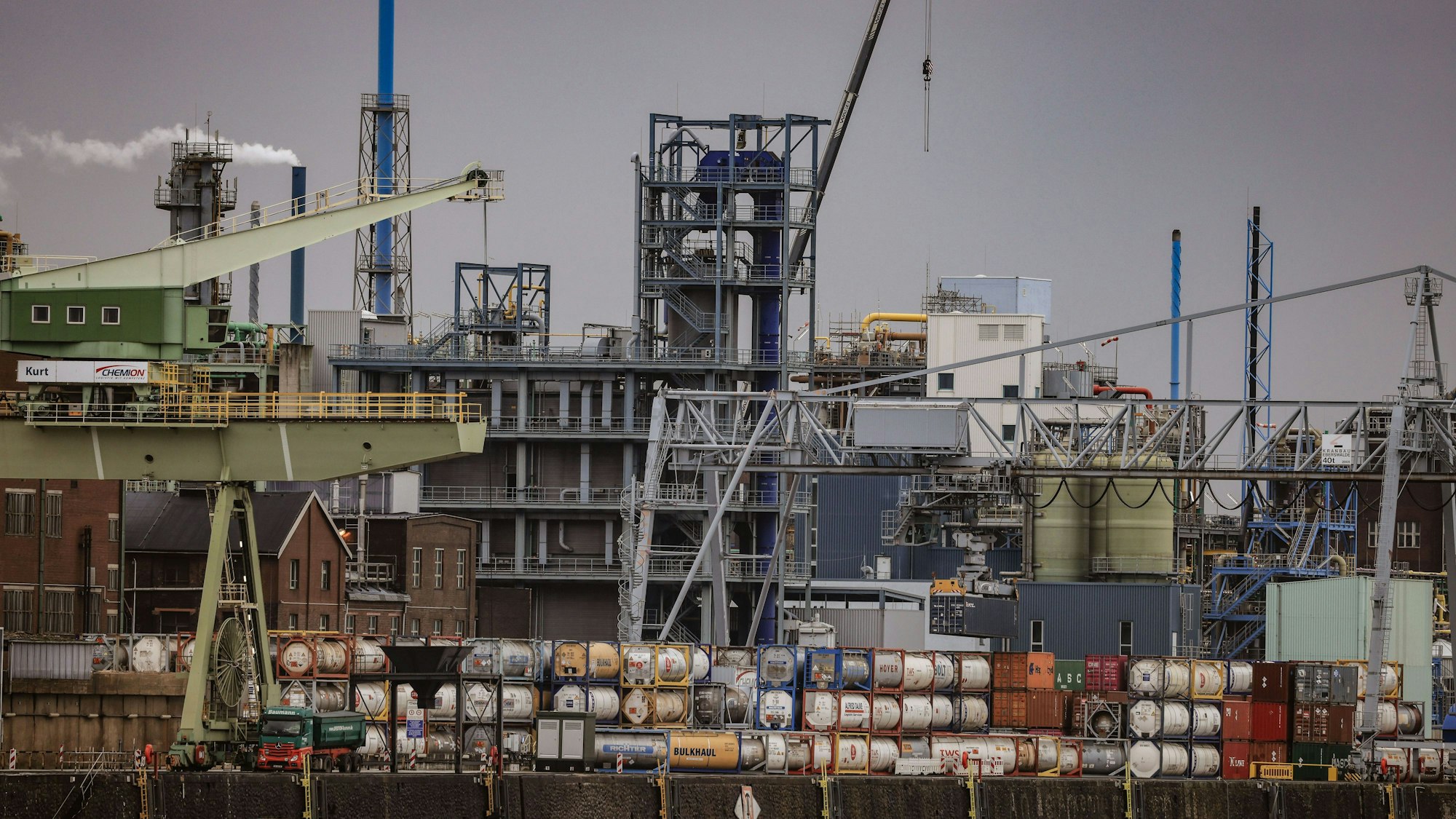 Container stapeln sich im Chempark Leverkusen vor Industrieanlagen.