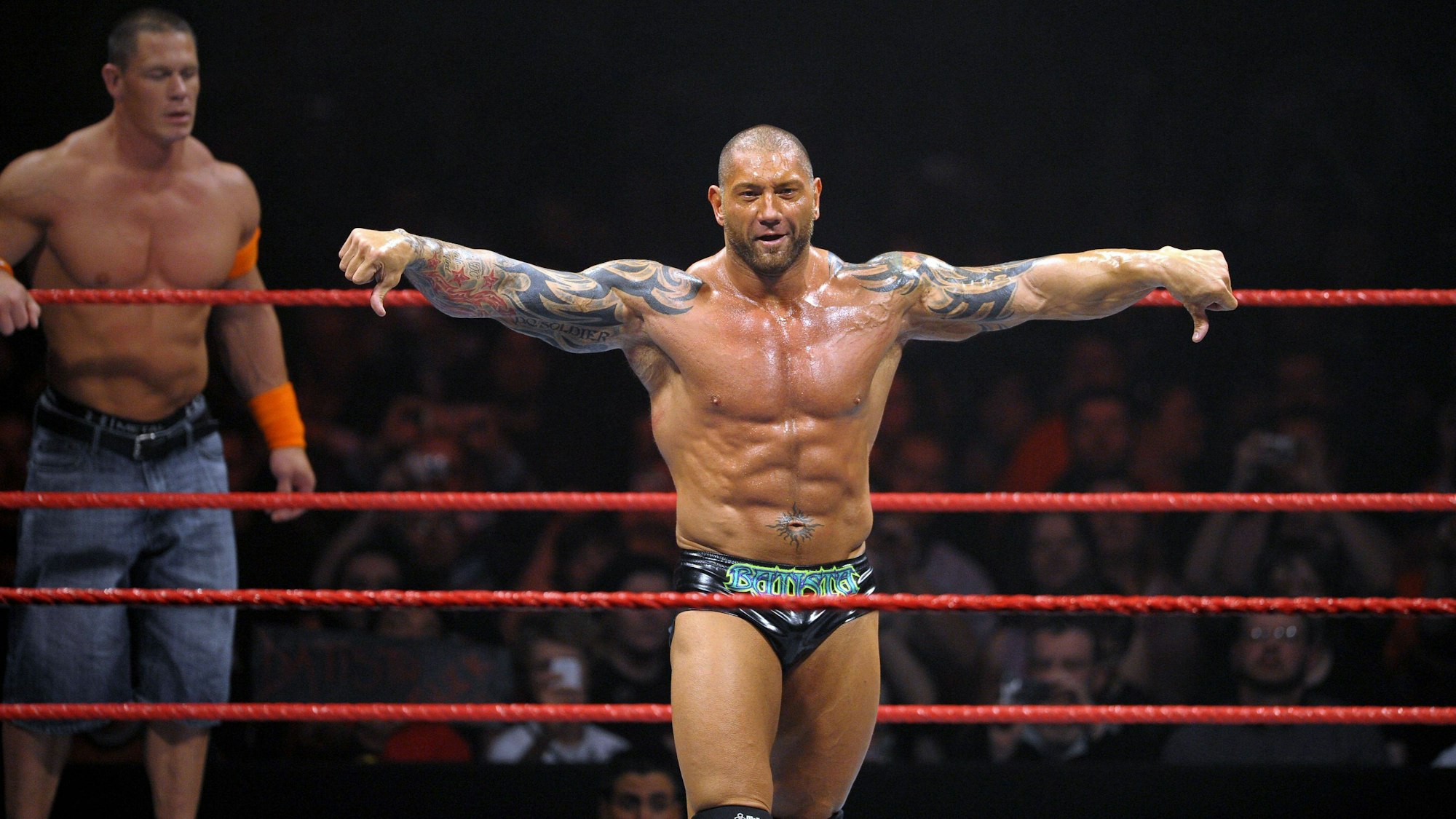 Batista bei einem WWE-Kampf im Ring. Hinter ihm steht John Cena.