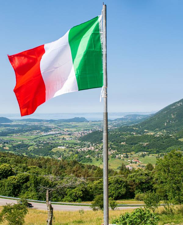 Eine italienische Flagge weht auf einem Balkon, in der Ferne ist der Gardasee zu sehen. Kriminelle in Italien haben Hunderte Menschen mit der Gründung eines fiktiven Staats und damit vermeintlich verbundenen Vorteilen um insgesamt Hunderttausende von Euro betrogen. (zu dpa "Betrüger ergaunern mit erfundenem Antarktisstaat rund 400.000 Euro ") +++ dpa-Bildfunk +++