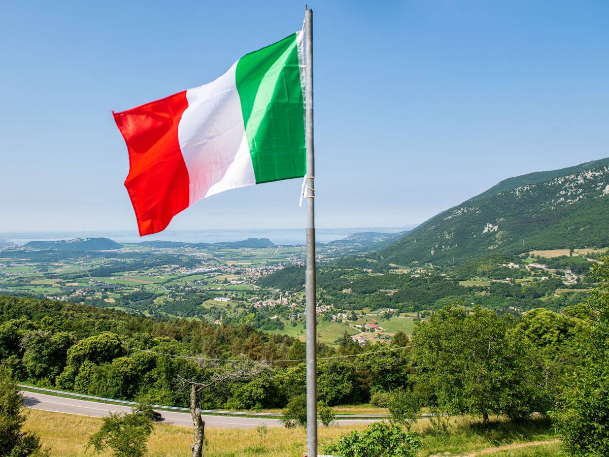Eine italienische Flagge weht auf einem Balkon, in der Ferne ist der Gardasee zu sehen. Kriminelle in Italien haben Hunderte Menschen mit der Gründung eines fiktiven Staats und damit vermeintlich verbundenen Vorteilen um insgesamt Hunderttausende von Euro betrogen. (zu dpa "Betrüger ergaunern mit erfundenem Antarktisstaat rund 400.000 Euro ") +++ dpa-Bildfunk +++
