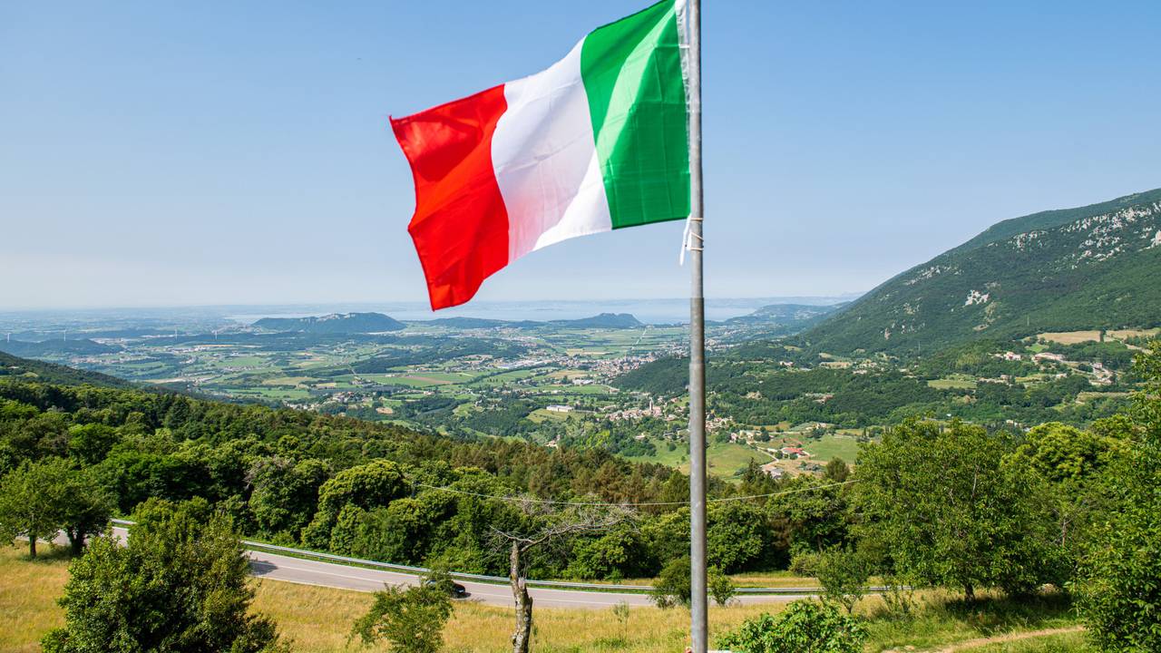 Eine italienische Flagge weht auf einem Balkon, in der Ferne ist der Gardasee zu sehen. Kriminelle in Italien haben Hunderte Menschen mit der Gründung eines fiktiven Staats und damit vermeintlich verbundenen Vorteilen um insgesamt Hunderttausende von Euro betrogen. (zu dpa "Betrüger ergaunern mit erfundenem Antarktisstaat rund 400.000 Euro ") +++ dpa-Bildfunk +++