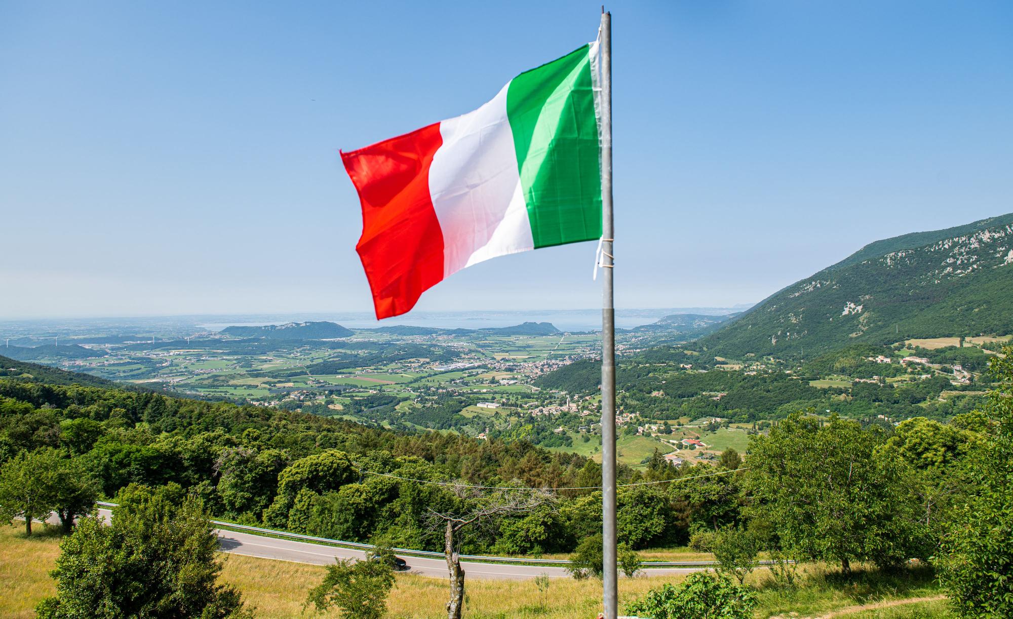 Eine italienische Flagge weht auf einem Balkon, in der Ferne ist der Gardasee zu sehen. Kriminelle in Italien haben Hunderte Menschen mit der Gründung eines fiktiven Staats und damit vermeintlich verbundenen Vorteilen um insgesamt Hunderttausende von Euro betrogen. (zu dpa "Betrüger ergaunern mit erfundenem Antarktisstaat rund 400.000 Euro ") +++ dpa-Bildfunk +++