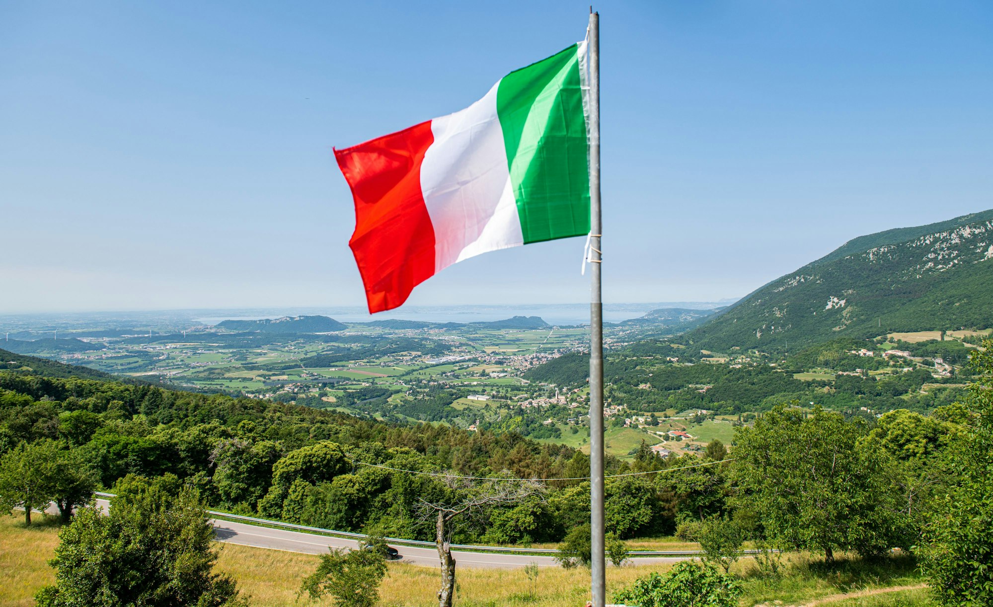 Eine italienische Flagge weht auf einem Balkon, in der Ferne ist der Gardasee zu sehen. Kriminelle in Italien haben Hunderte Menschen mit der Gründung eines fiktiven Staats und damit vermeintlich verbundenen Vorteilen um insgesamt Hunderttausende von Euro betrogen. (zu dpa "Betrüger ergaunern mit erfundenem Antarktisstaat rund 400.000 Euro ") +++ dpa-Bildfunk +++