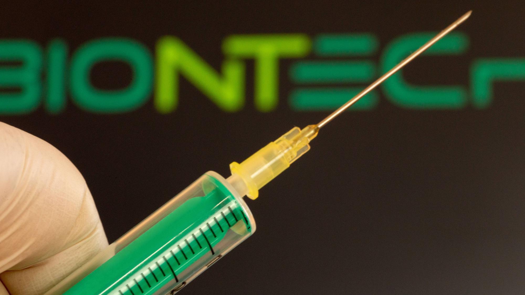 Nahaufnahme einer Injektionsnadel, im Hintergrund das Logo von Biontech.