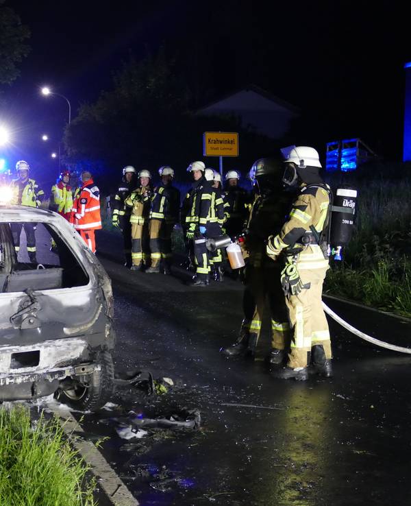 Feuerwehrfahrleute stehen bei einem ausgebrannten Fahrzeug auf der Autobahn.