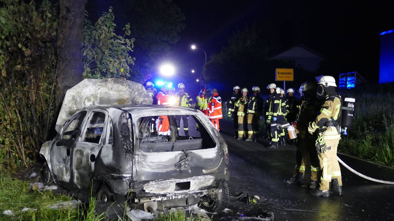 Feuerwehrfahrleute stehen bei einem ausgebrannten Fahrzeug auf der Autobahn.
