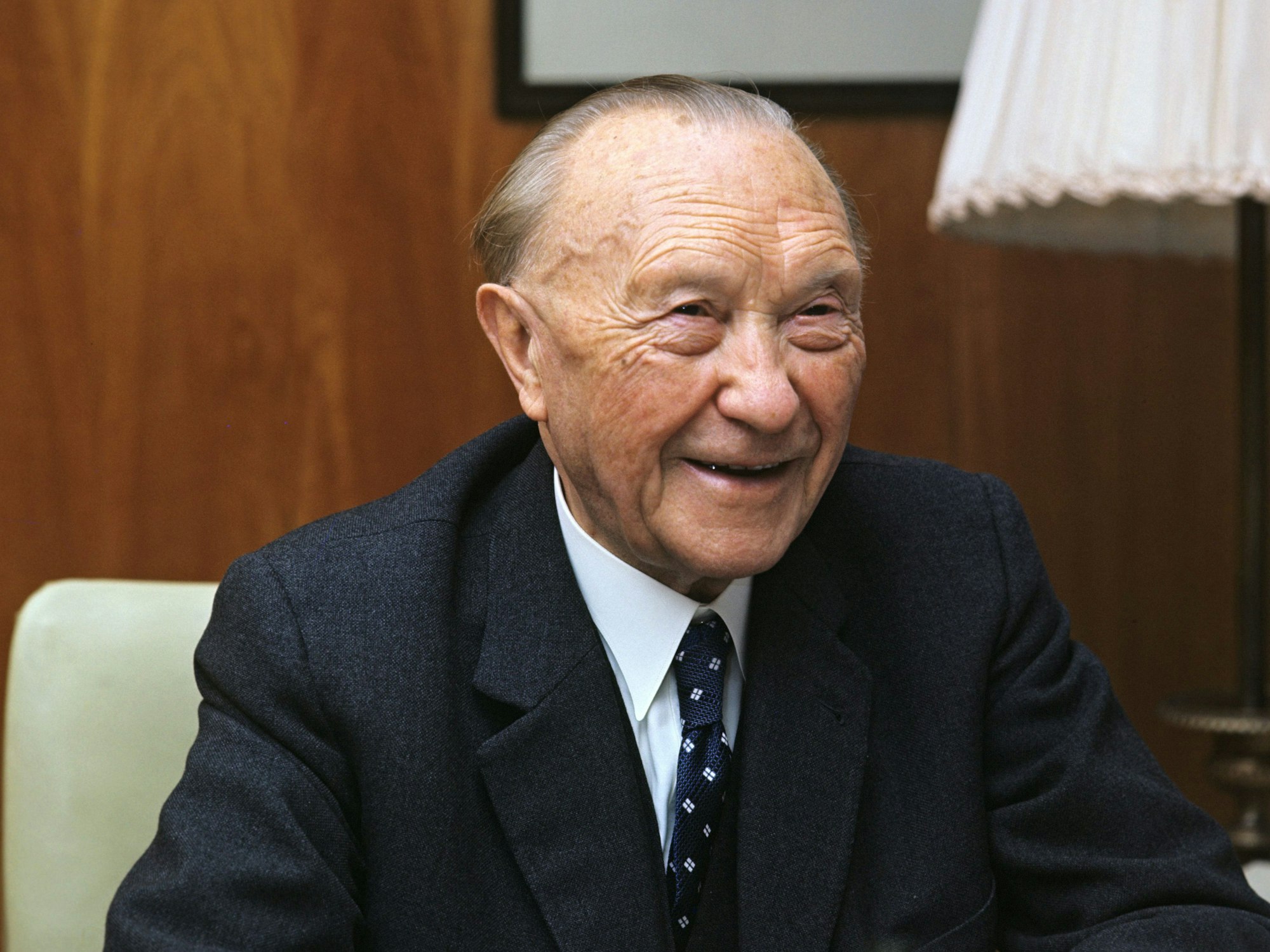 Konrad Adenauer sitzt lächelnd auf einem Stuhl.