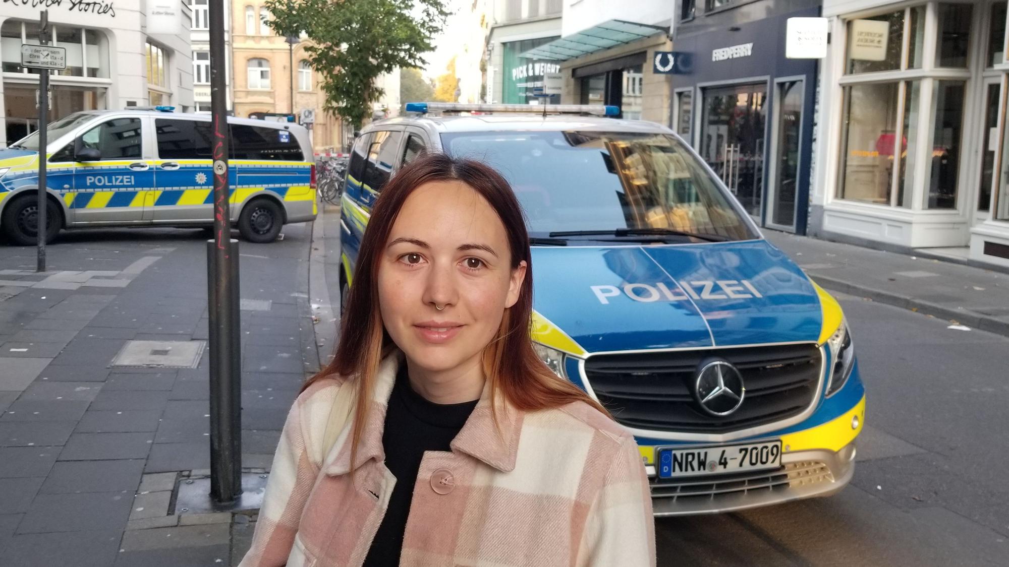 Eine Frau steht auf der Ehrenstraße in Köln vor zwei Polizeifahrzeugen.