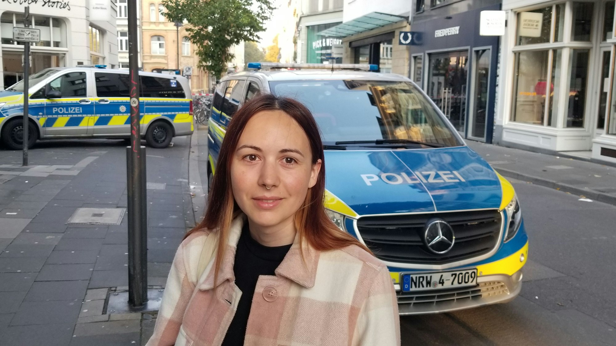 Eine Frau steht auf der Ehrenstraße in Köln vor zwei Polizeifahrzeugen.