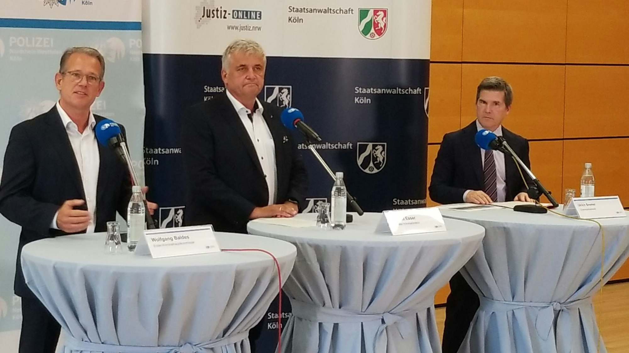 Drei Männer stehen bei einer Pressekonferenz an Rednerpulten.