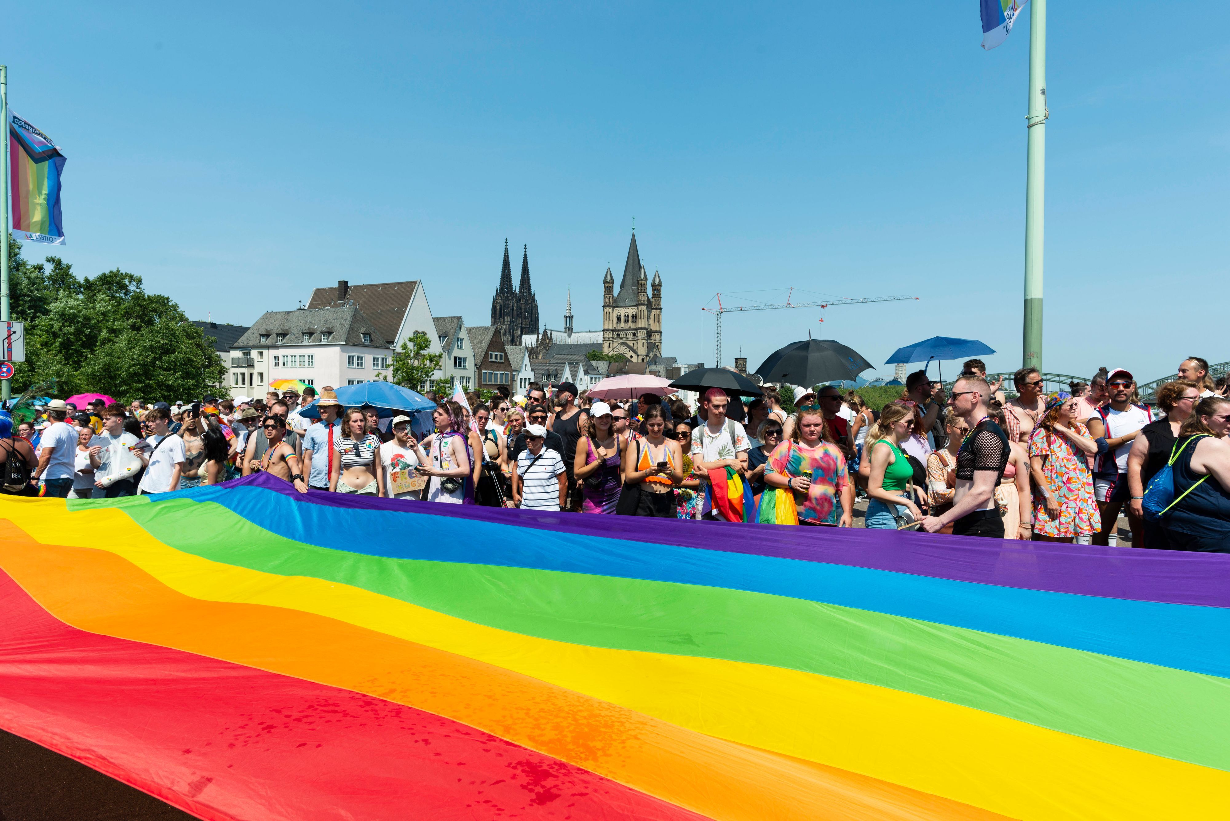 Menschen stehen hinter einer riesigen Regenbogenfahne.