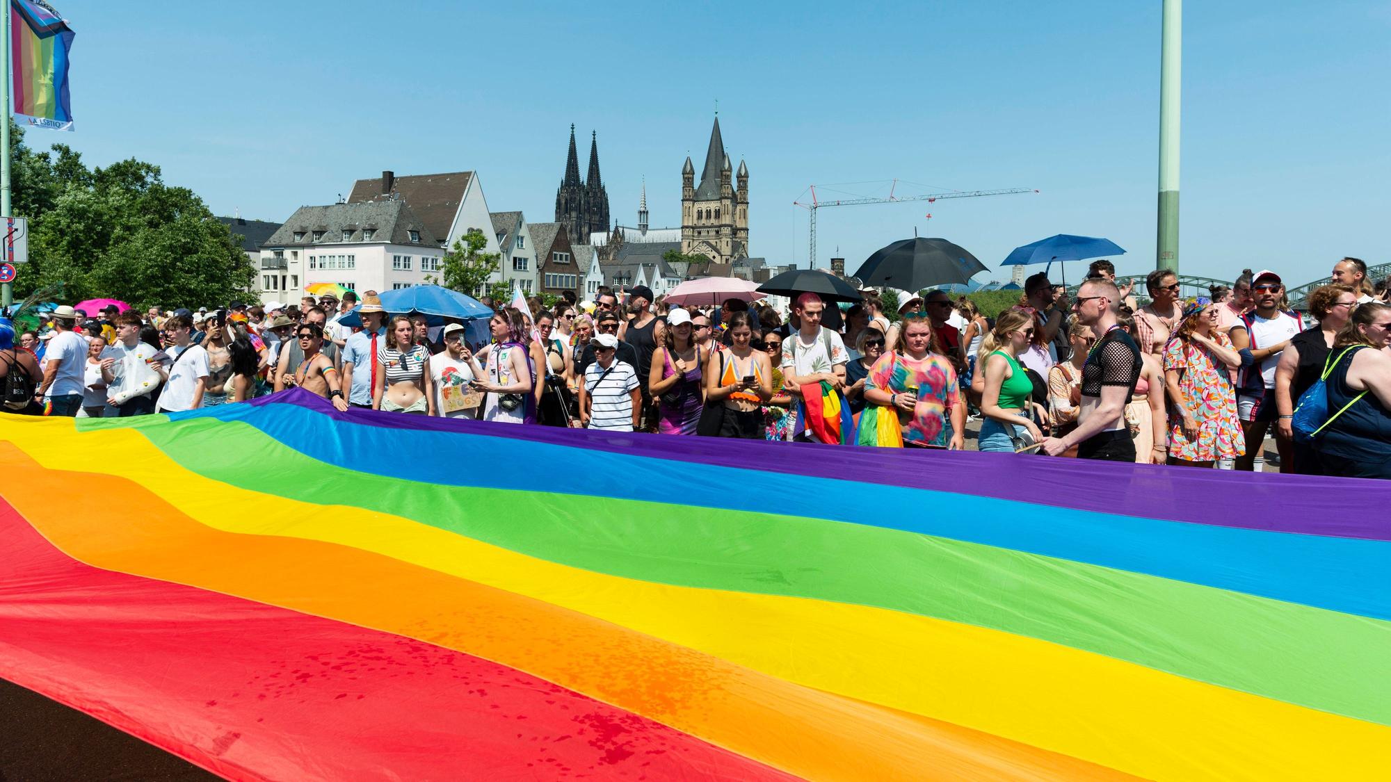 Menschen stehen hinter einer riesigen Regenbogenfahne.