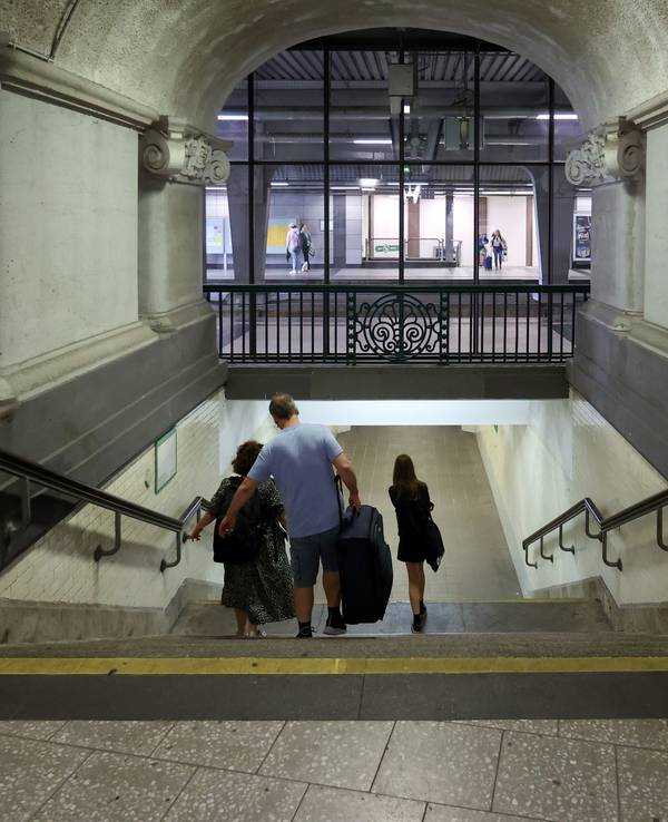 Drei Menschen gehen im Bahnhof Köln Messe/Deutz mit ihrem Gepäck eine Treppe herunter.