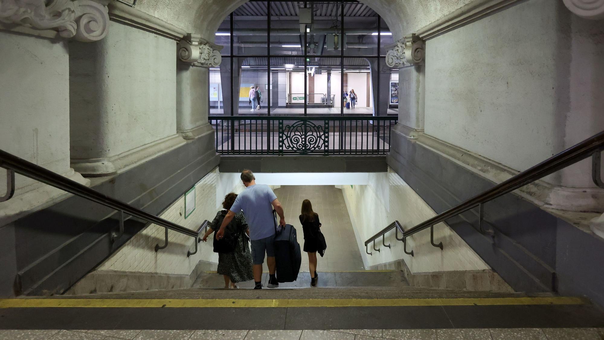 Drei Menschen gehen im Bahnhof Köln Messe/Deutz mit ihrem Gepäck eine Treppe herunter.