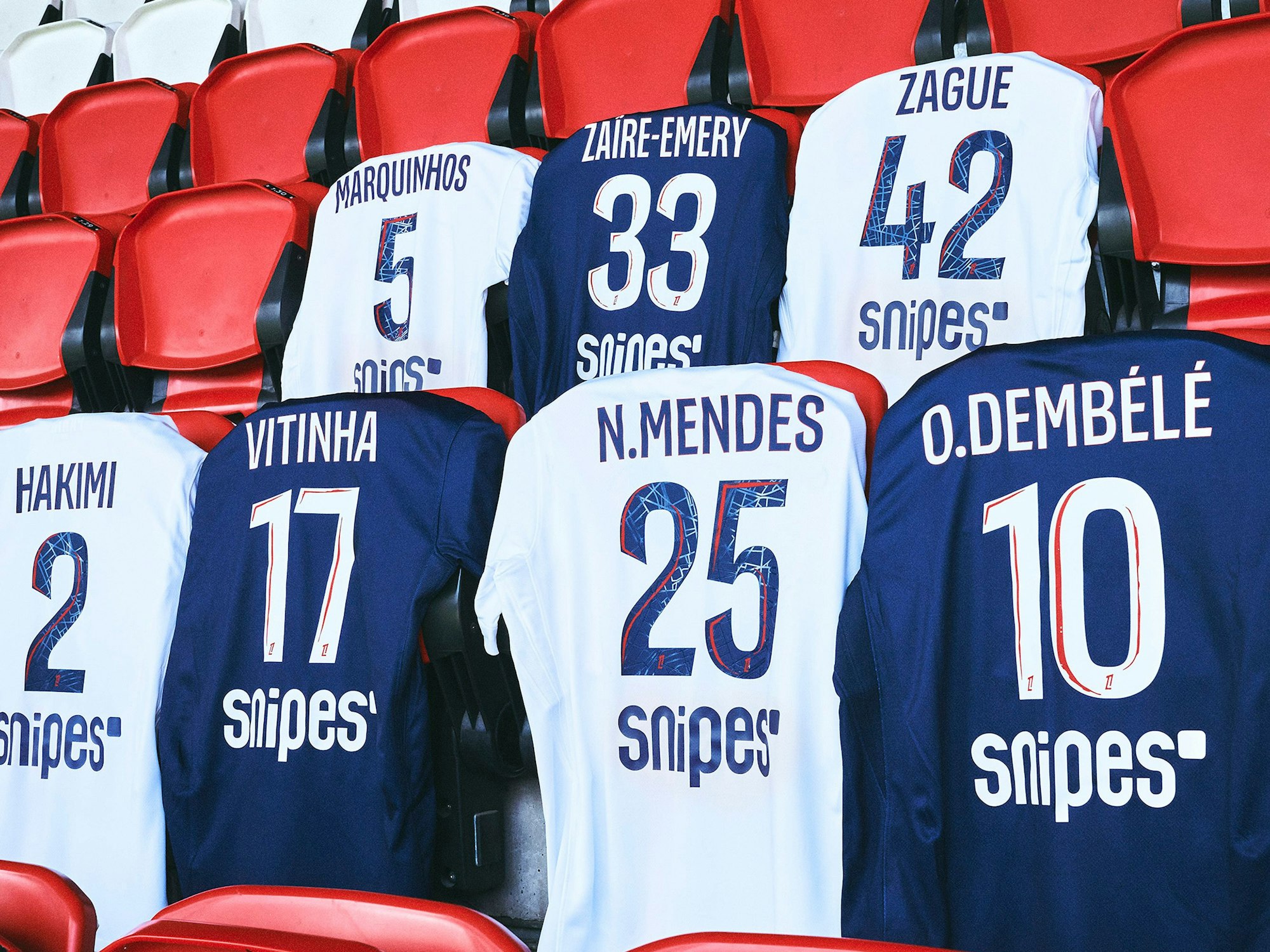 Mehrere Trikots von Paris St. Germain hängen auf einer Tribüne.