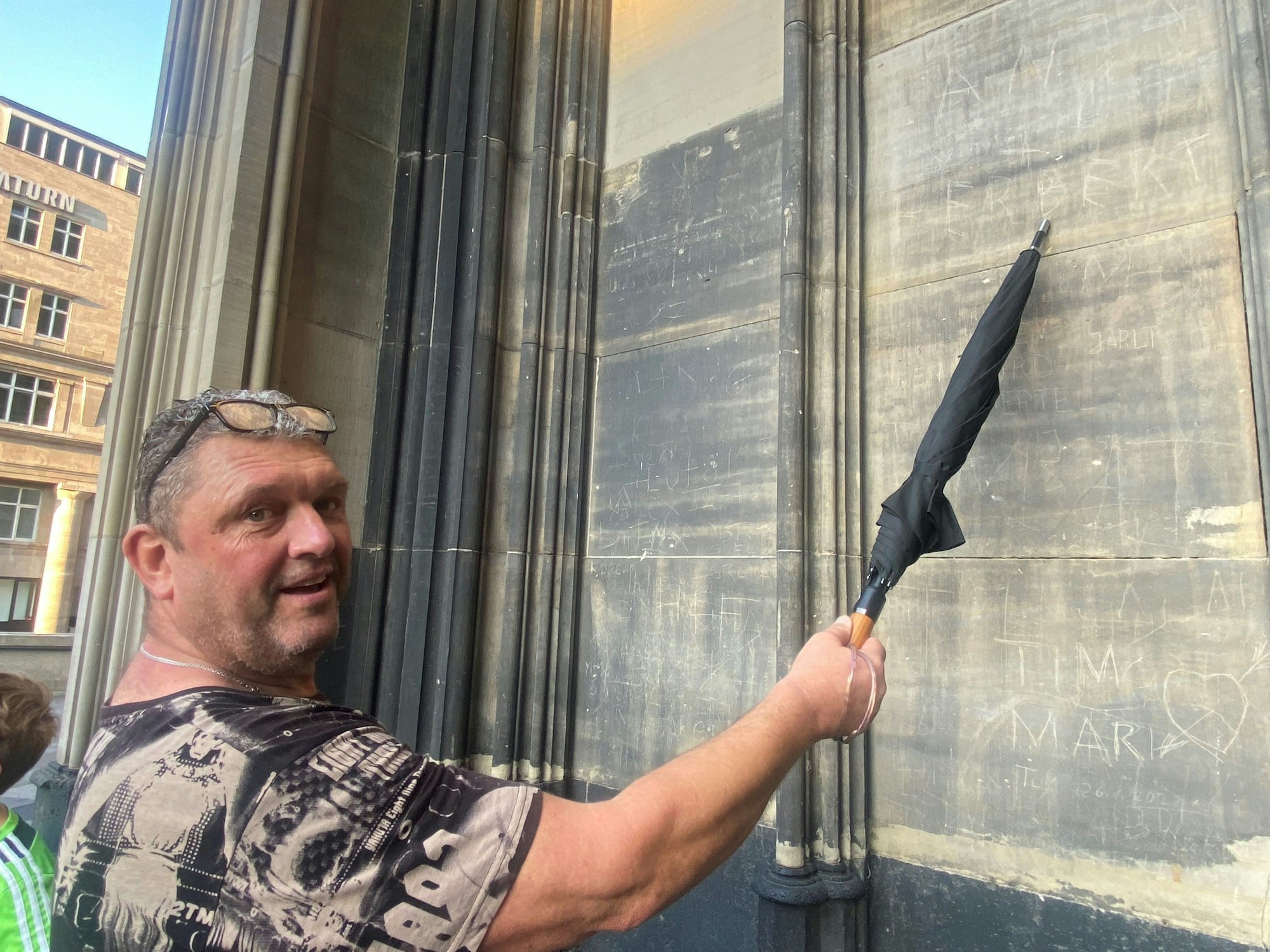 Herbert Schwan zeigt mit einem Schirm auf eine gekritzelte Schrift am Kölner Dom.