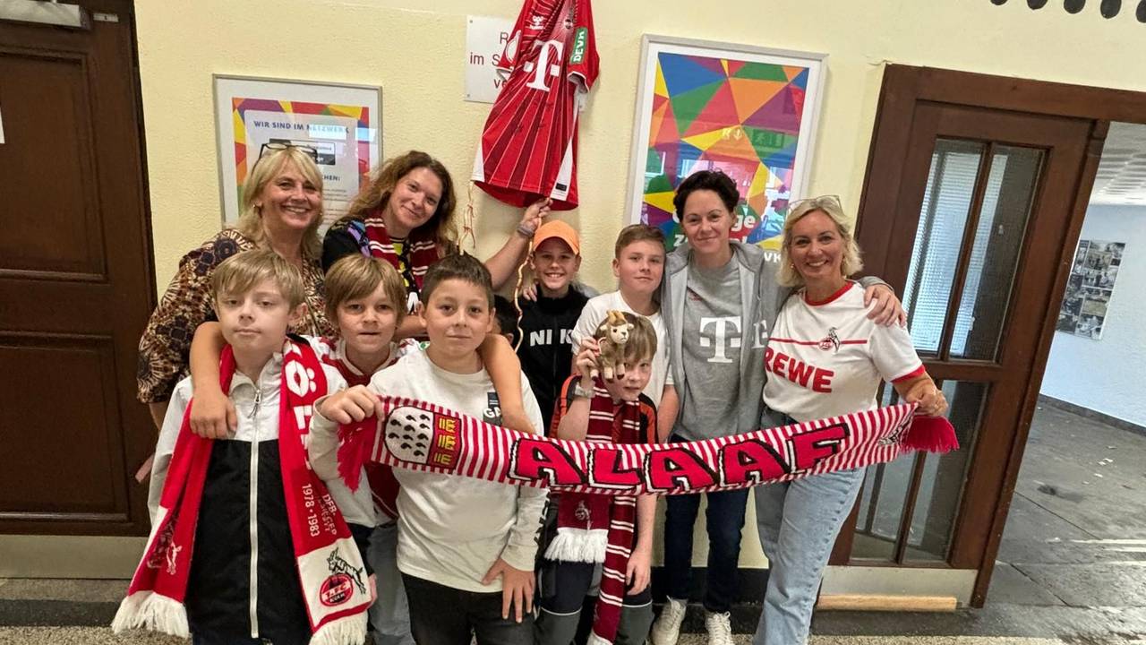 Einige Frauen und einige Kinder stehen in Kleidung des 1. FC Köln für ein Gruppenbild zusammen.