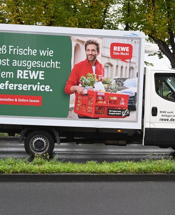 Ein Fahrzeug des Rewe Lieferservice fährt auf einer Straße.