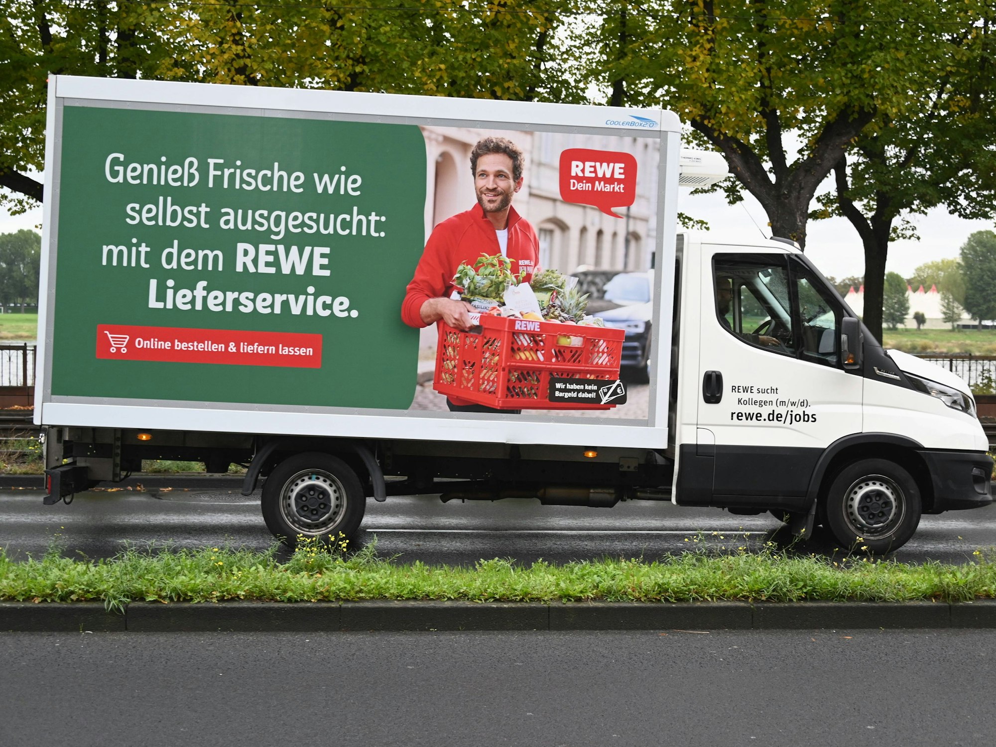 Ein Fahrzeug des Rewe Lieferservice fährt auf einer Straße.