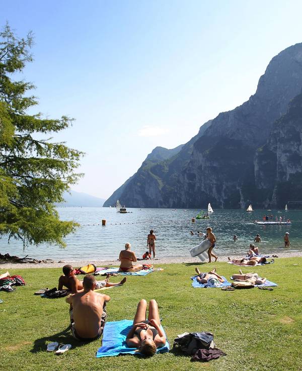 Touris und Einheimische nehmen am Strand von Riva del Garda ein Sonnenbad