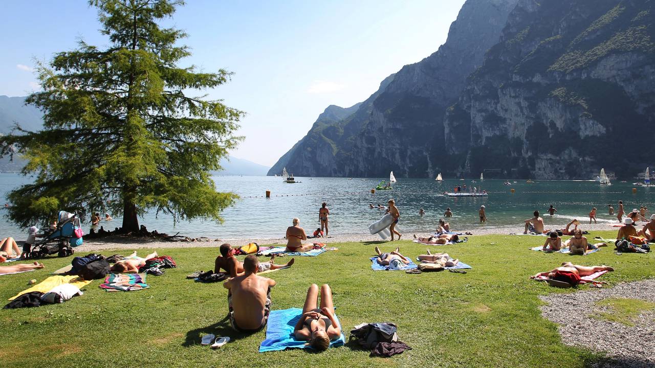 Touris und Einheimische nehmen am Strand von Riva del Garda ein Sonnenbad