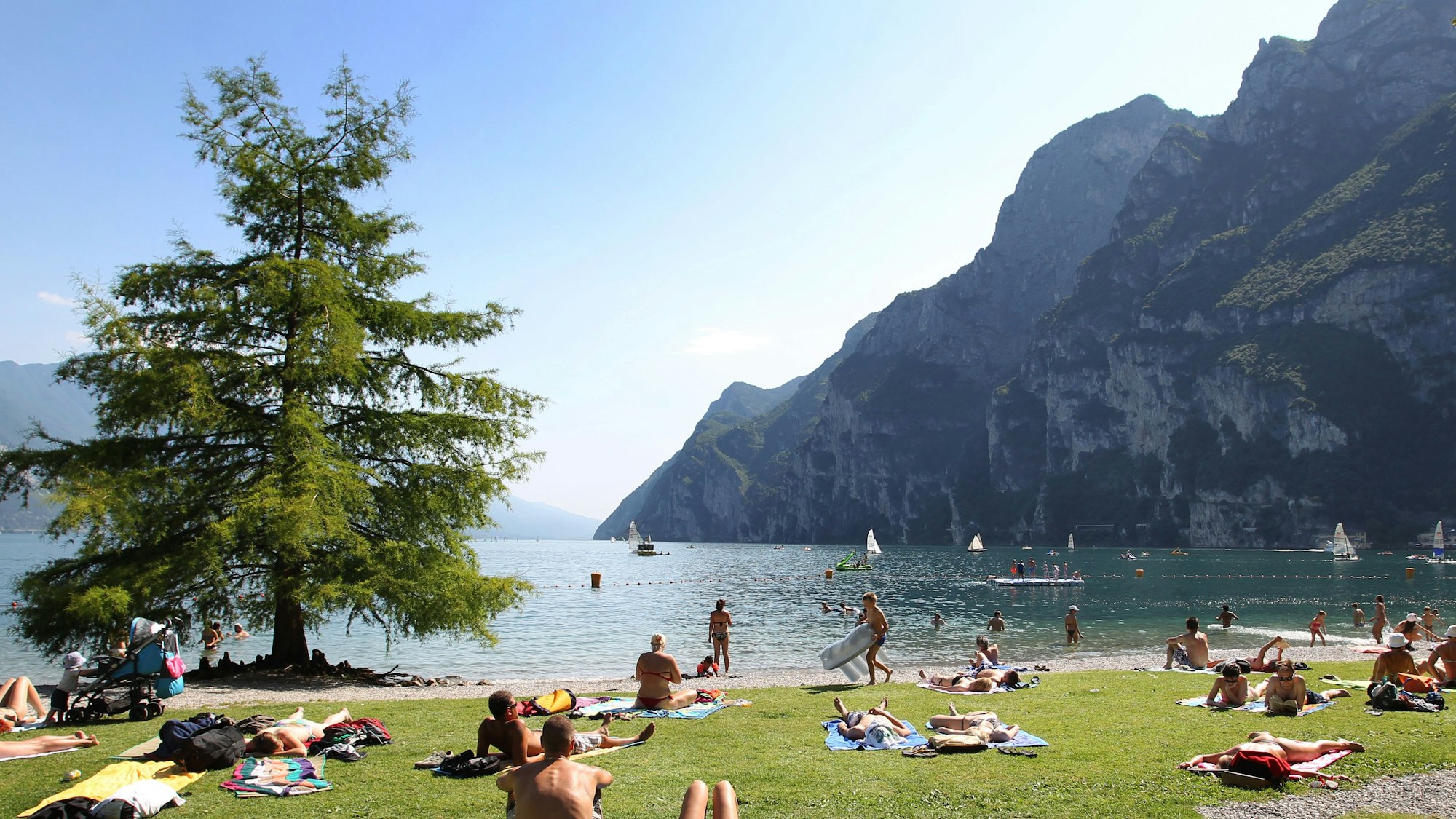 Touris und Einheimische nehmen am Strand von Riva del Garda ein Sonnenbad