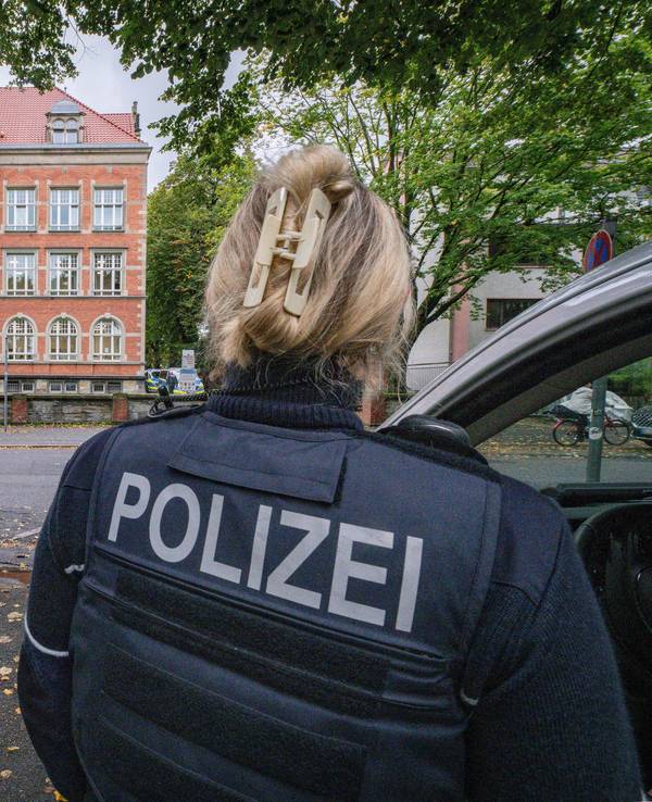 Einsatzfahrzeuge und eine Polizistin stehen vor einem großen Gebäude.
