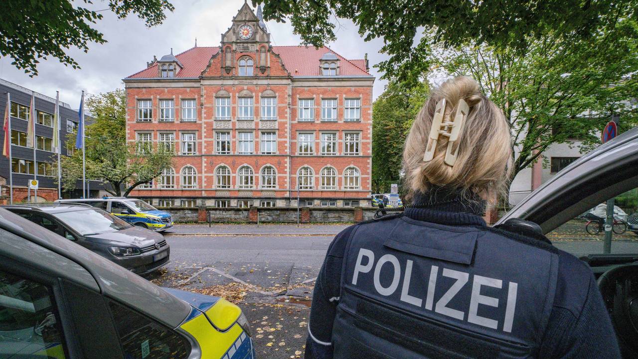 Einsatzfahrzeuge und eine Polizistin stehen vor einem großen Gebäude.