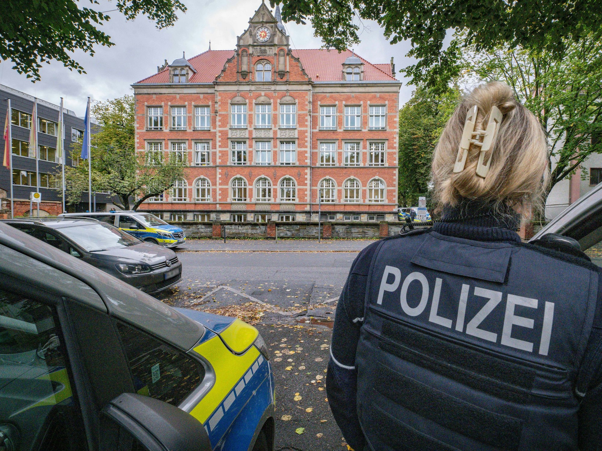 Einsatzfahrzeuge und eine Polizistin stehen vor einem großen Gebäude.