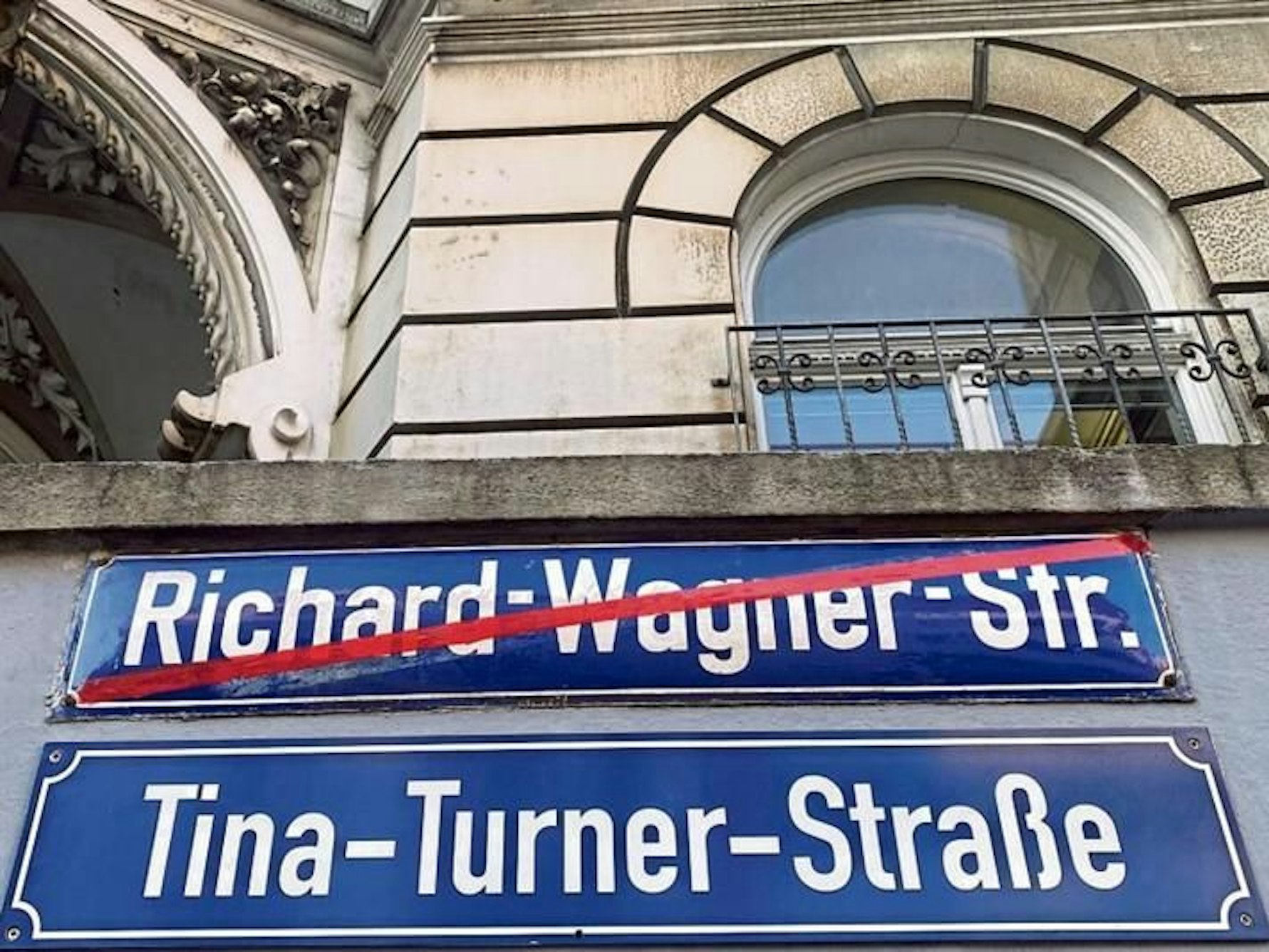 Zwei Straßenschilder hängen an einer Wand.