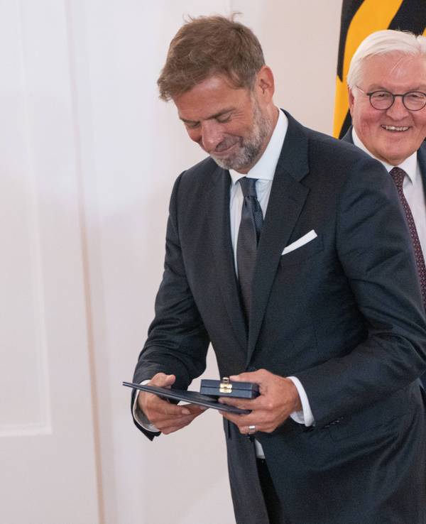 Jürgen Klopp betrachtet stolz seinen Verdienstorden, im Hintergrund lächelt Frank-Walter Steinmeier.