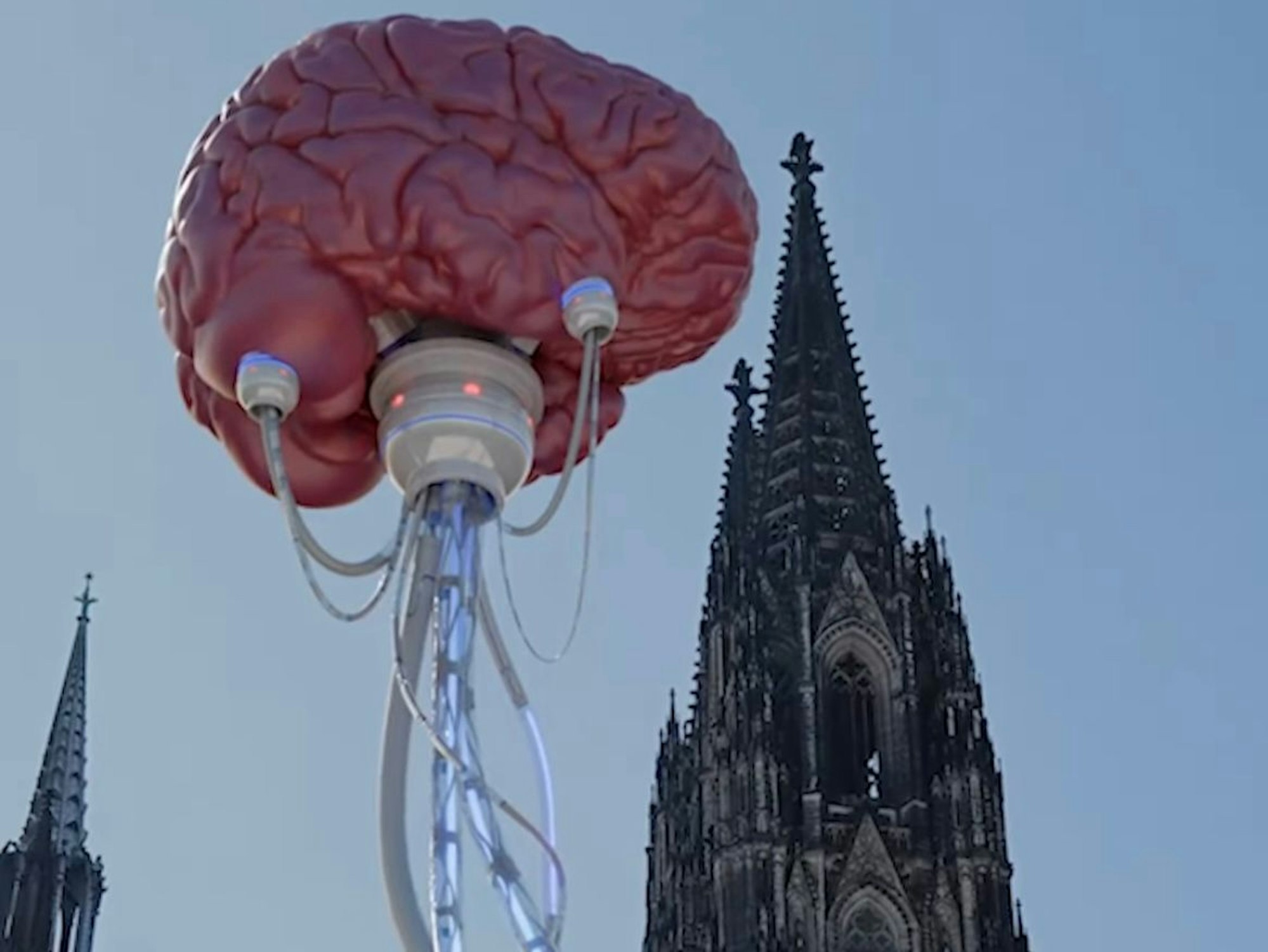 Vor dem Kölner Dom schwebt ein Gehirn, das an Kabeln angeschlossen ist.