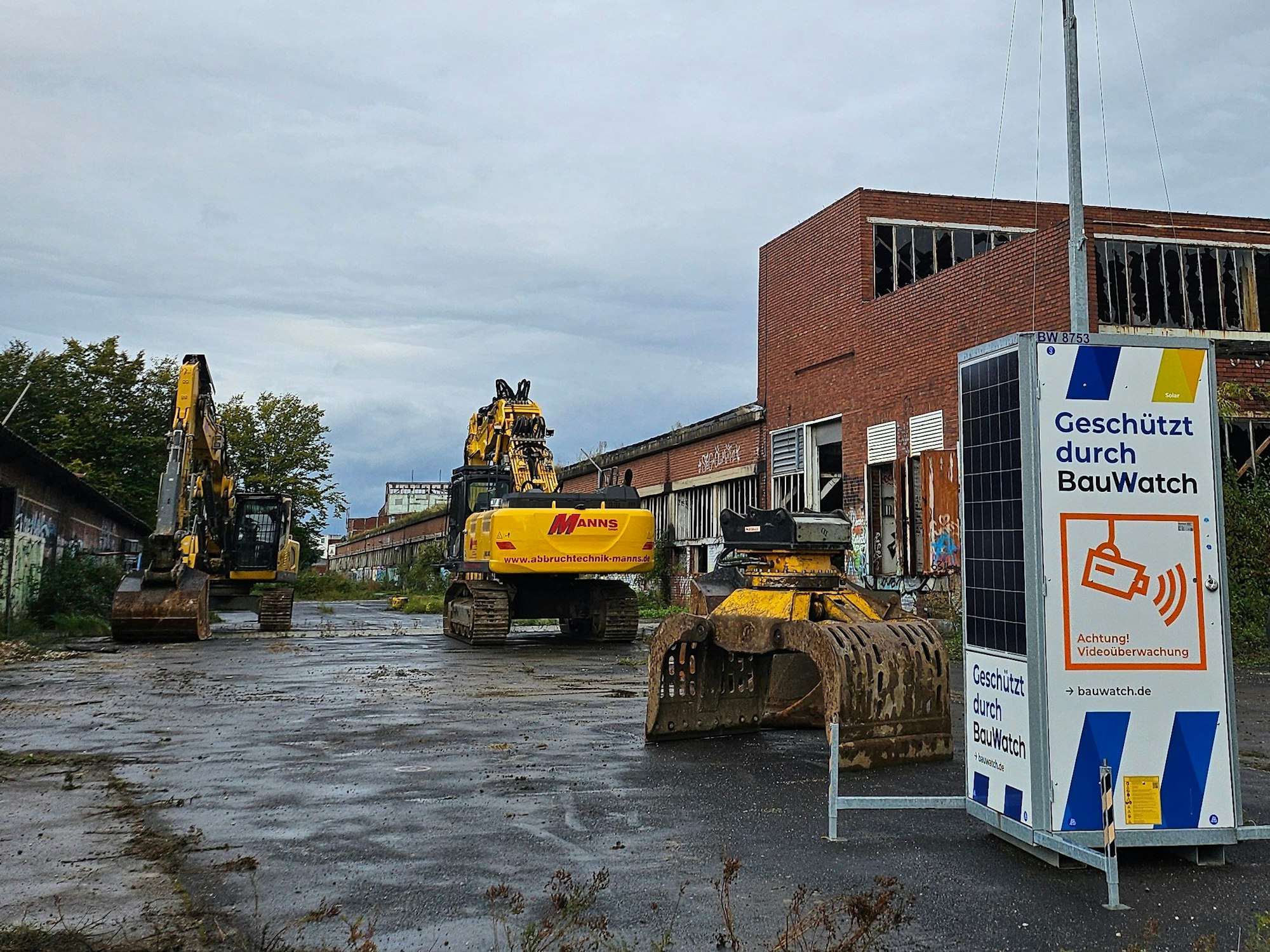 Auf einem Gelände mit verfallenen Gebäuden stehen zwei Bagger.