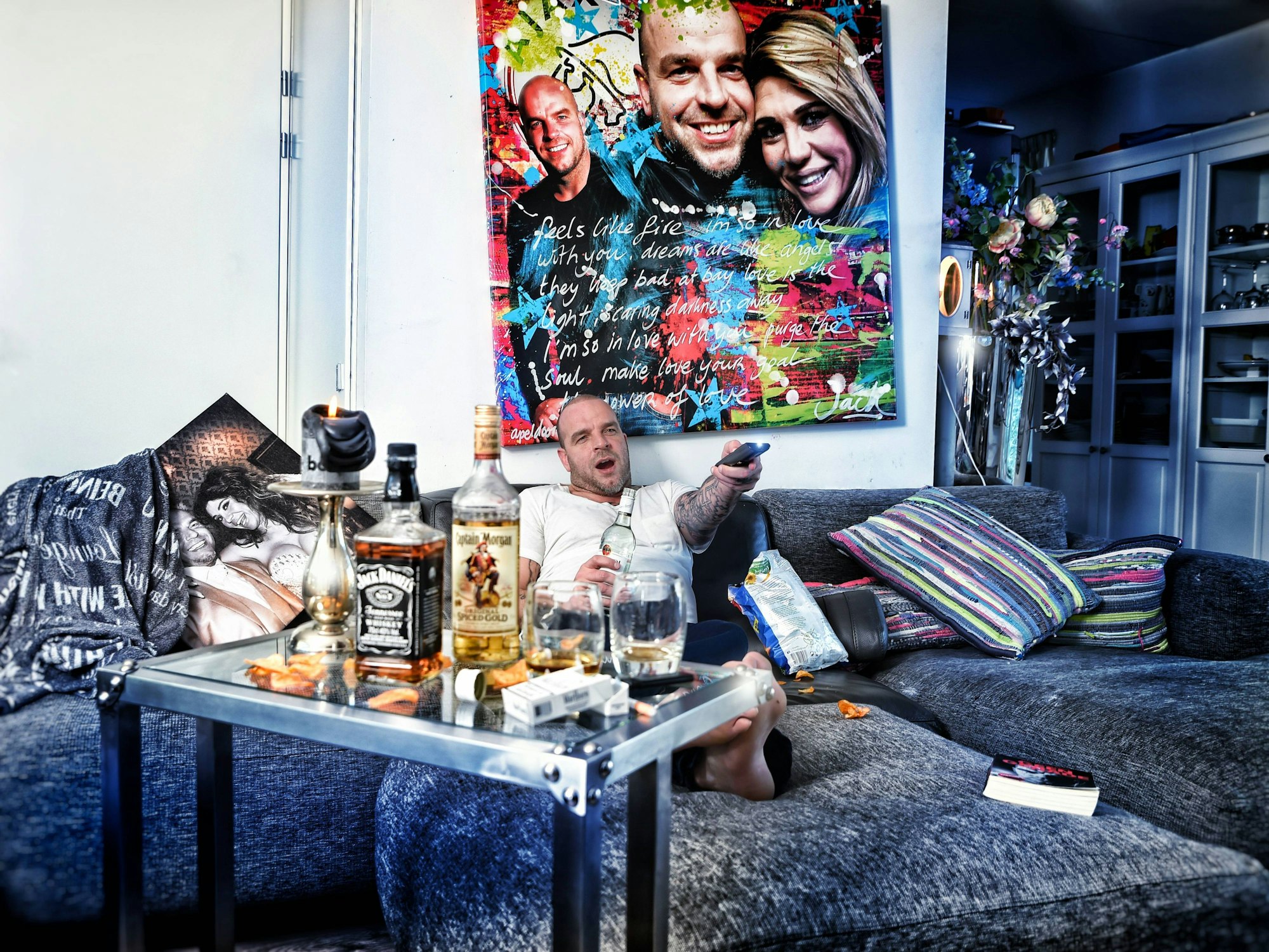 Andy van der Meyde liegt bei einem selbstironischen Fotoshooting auf dem Sofa in seinem Haus, vor ihm stehen Schnapsflaschen.