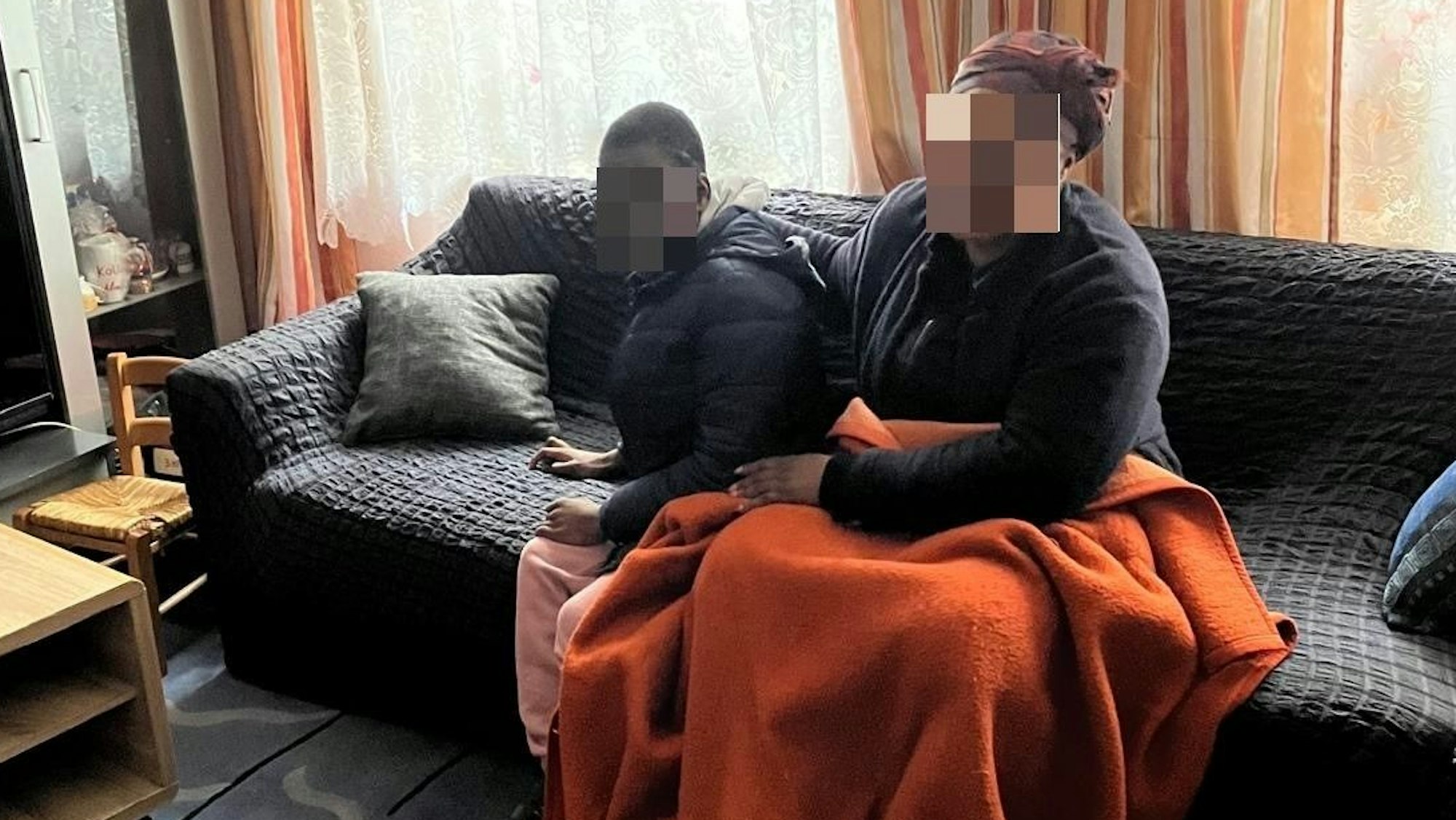 Eine Frau und ein Kind sitzen auf einem Sofa, sie haben eine Decke über den Beinen.