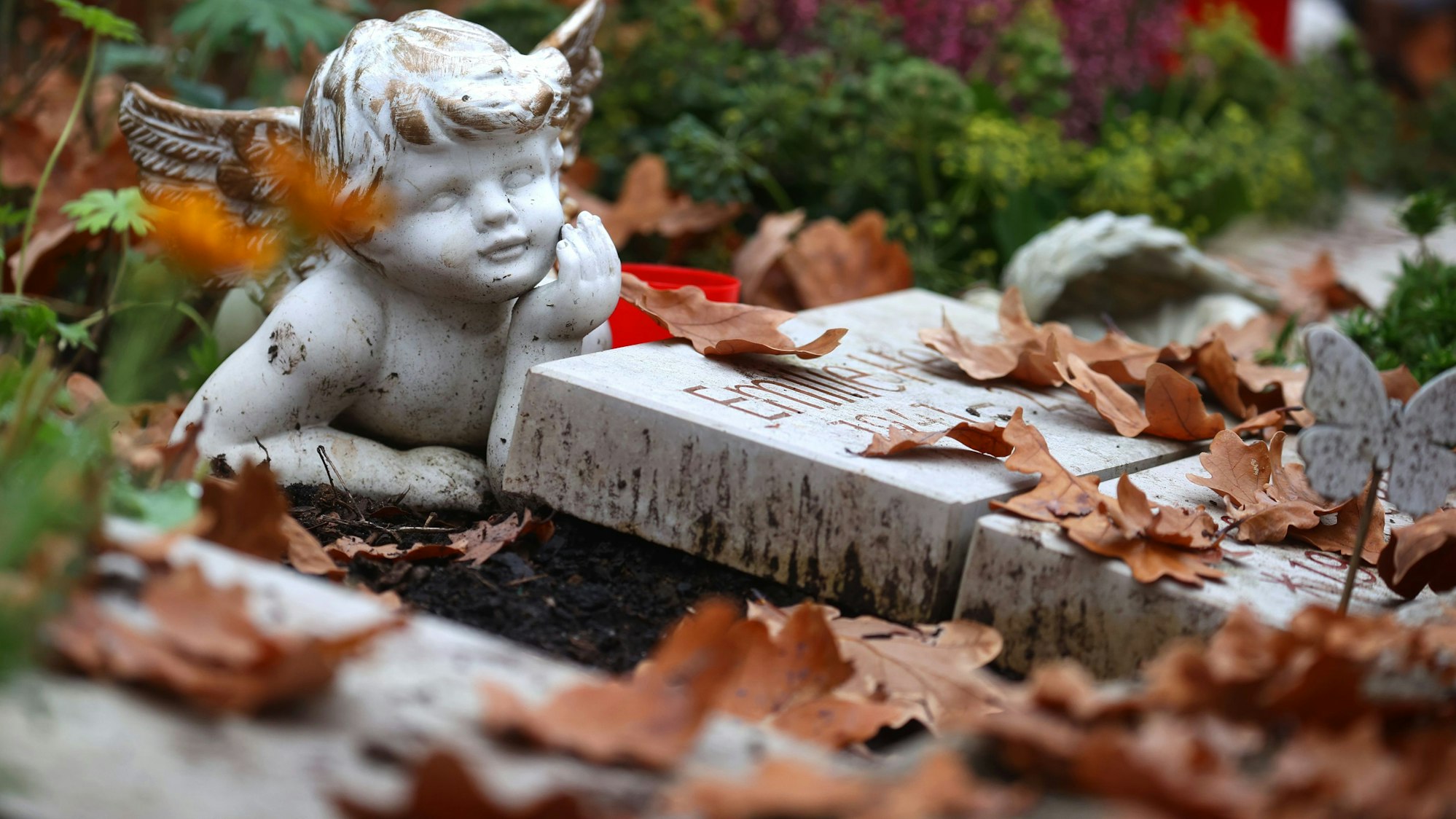 Eine Engelsfigur liegt auf dem Zentralfriedhof auf einem Grab zwischen Herbstlaub. +++ dpa-Bildfunk +++