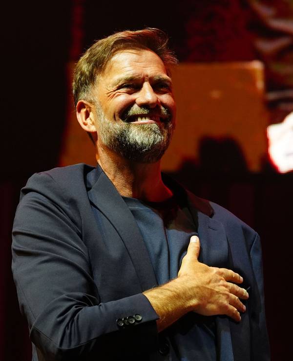 Jürgen Klopp fasst sich bei einer Veranstaltung mit der rechten Hand an sein Herz, während er breit grinst,