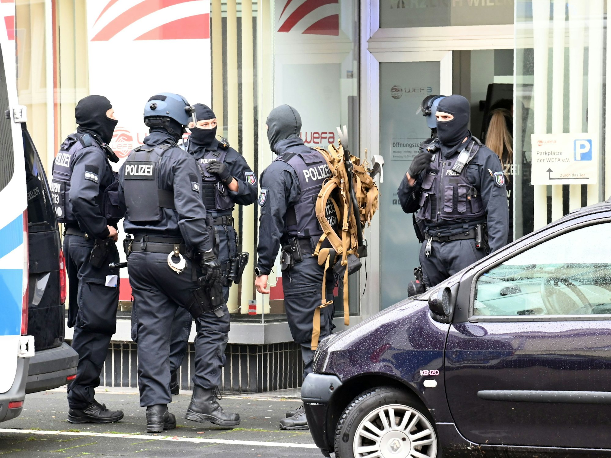 Fünf vermummte Einsatzkräfte stehen vor einer Eingangstür eines Gebäudes.