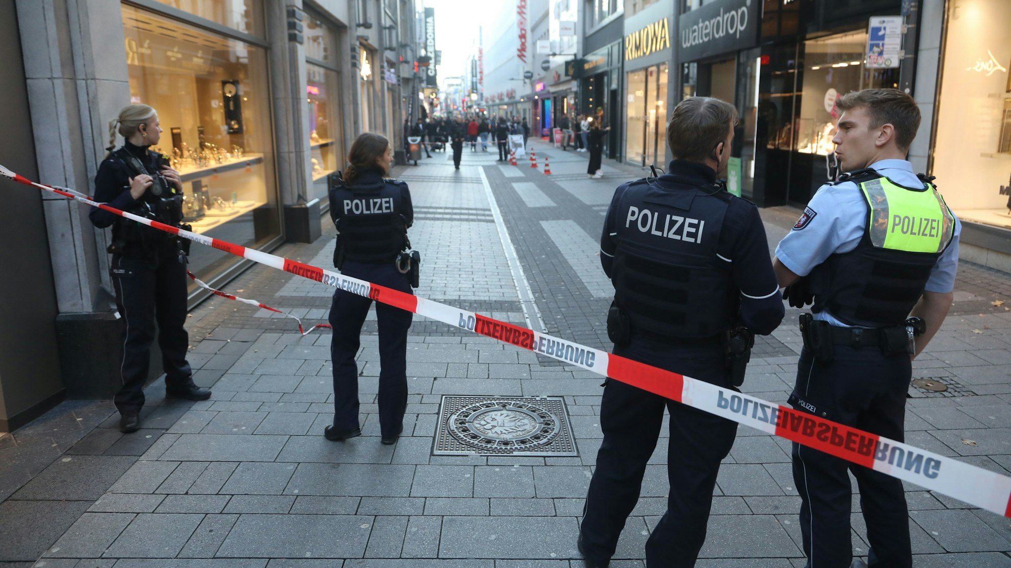 Ein Bereich einer Fußgängerzone ist mit Polizeiflatterband abgesperrt, dahinter stehen zwei Polizistinnen und zwei Polizisten.