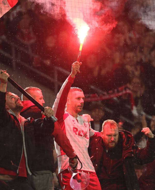 Lukas Podolski mit Pyro in der Hand bei den Fans auf dem Zaun im Stadion.