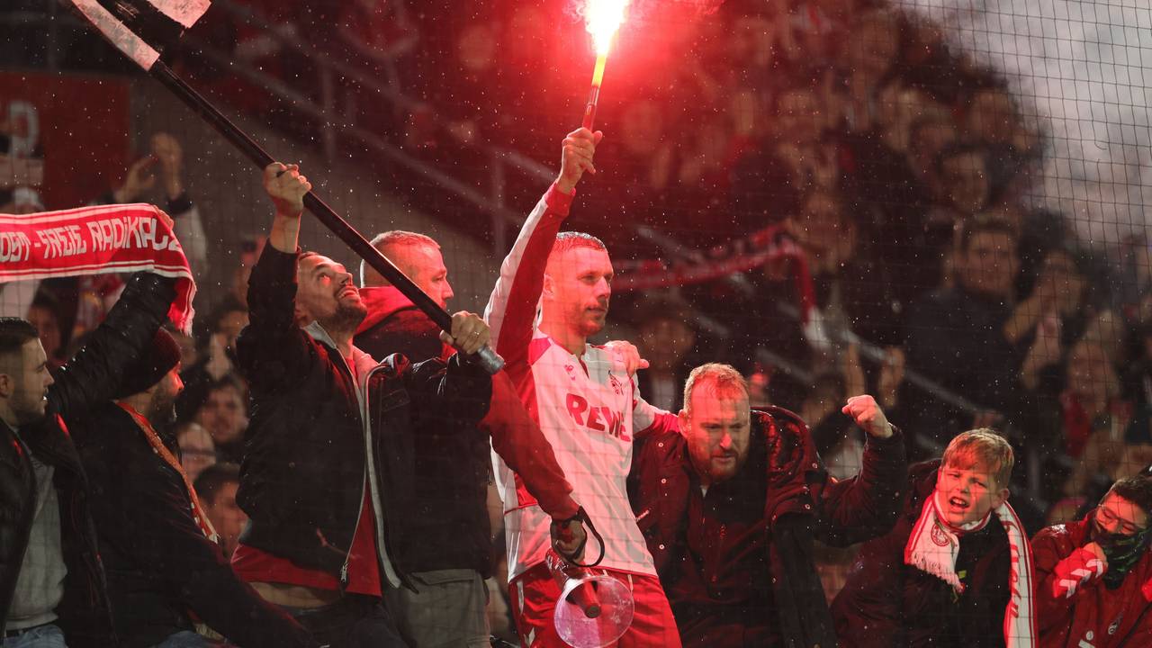 Lukas Podolski mit Pyro in der Hand bei den Fans auf dem Zaun im Stadion.