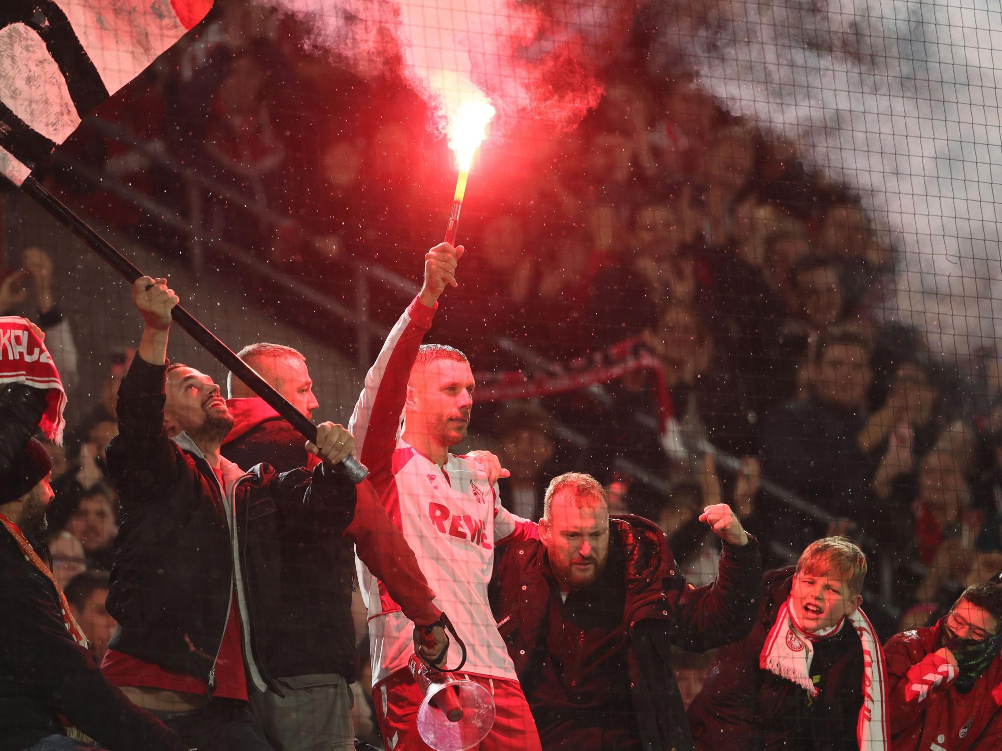 Lukas Podolski mit Pyro in der Hand bei den Fans auf dem Zaun im Stadion.