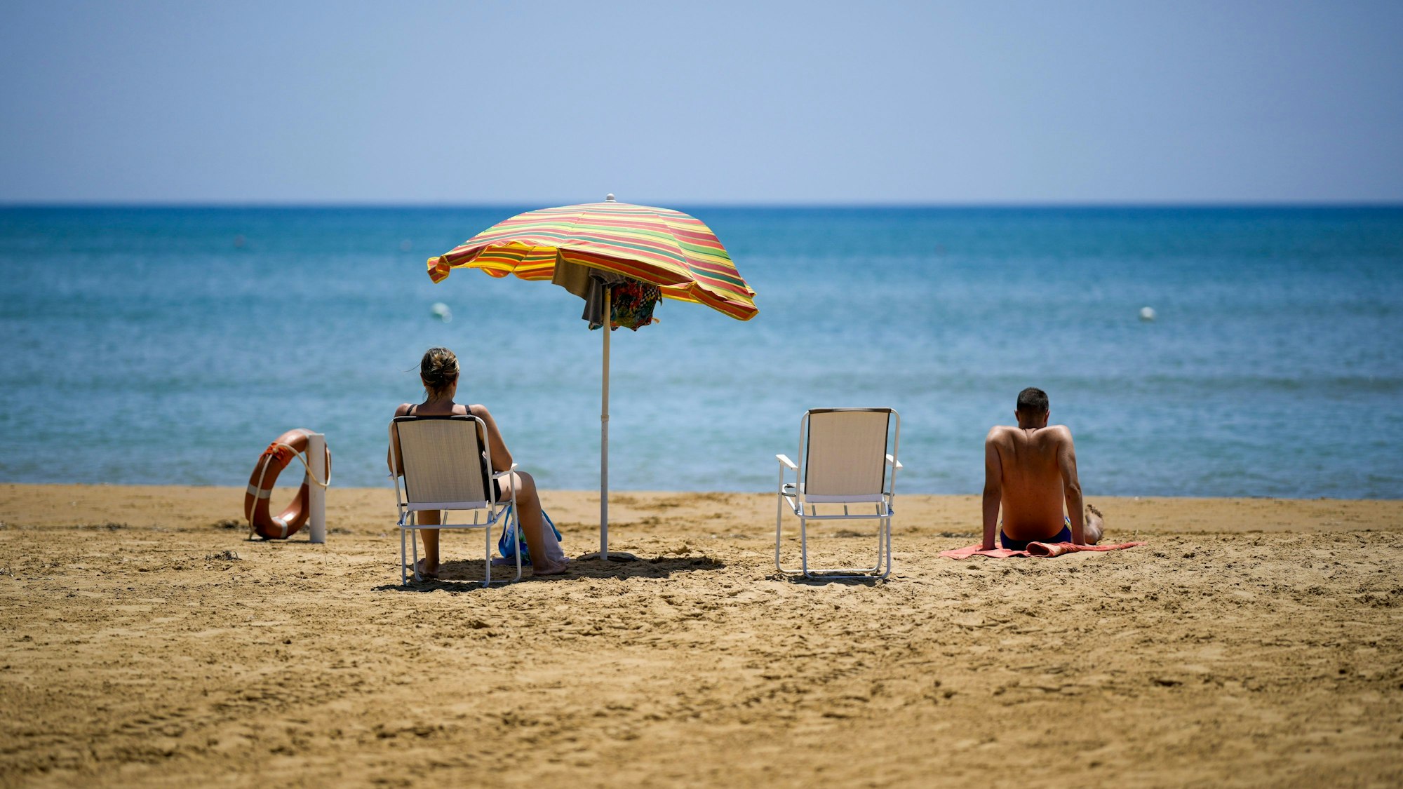 Eine Frau und ein Mann sitzen an einem Strand und schauen auf das Meer.