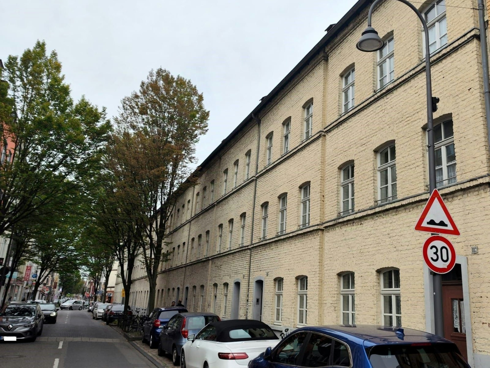 Eine Häuserfront zieht sich die ganze Straße entlang, davor parken Autos.