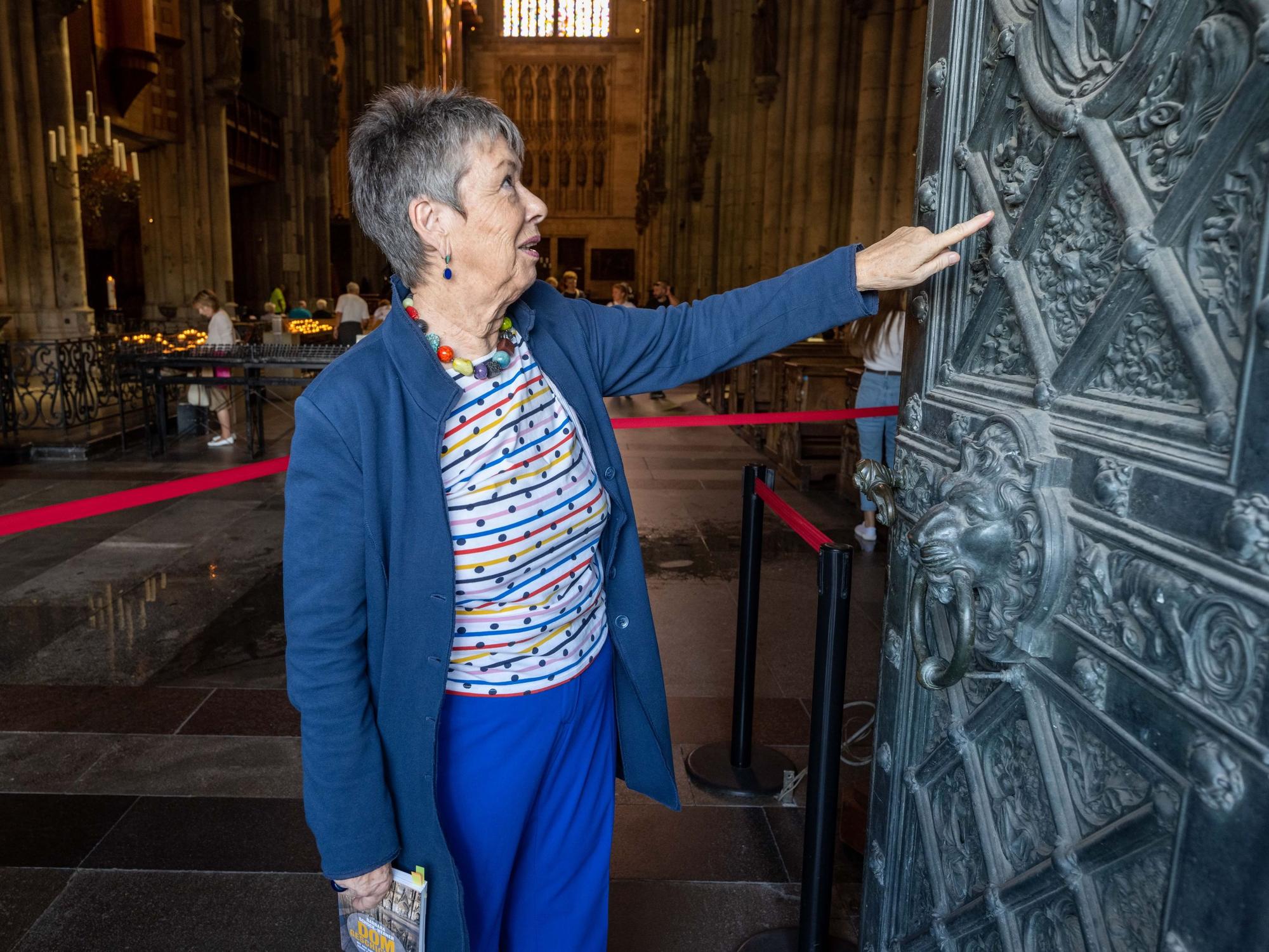 Barbara Schock-Werner fasst an eine offene Seitentür des Kölner Doms und betrachtet die Kunstwerke.