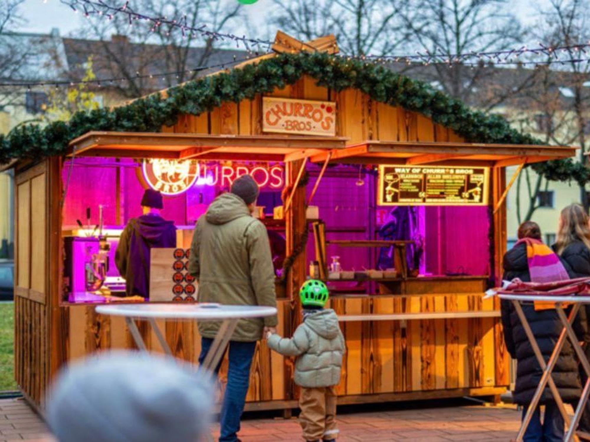 Gäste stehen vor einer Hütte am Sülzer Weihnachtsdorf.