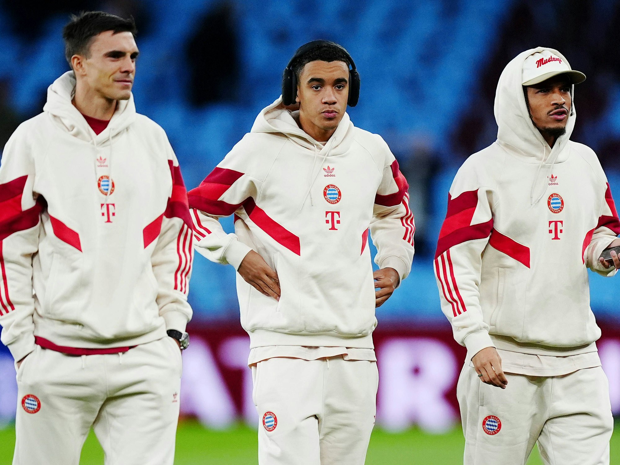 Joao Palhinha, Jamal Musiala und Leroy Sané posieren in den weißen Champions-League-Trainingsanzügen des FC Bayern.
